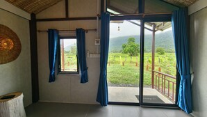 A room with a large sliding glass door to a balcony, a woven ceiling, and a small window with blue curtains.