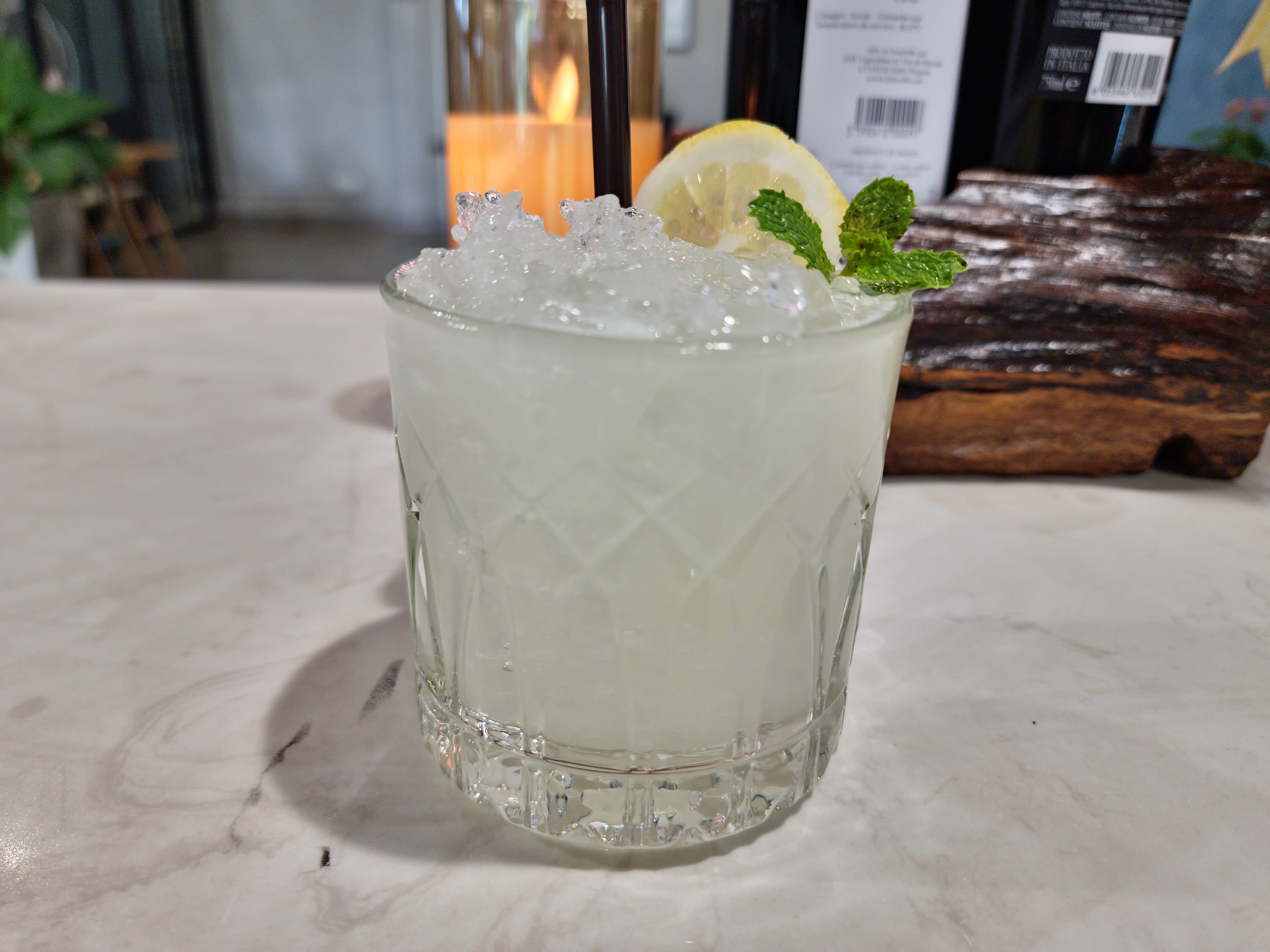 Un vaso transparente con cubitos de hielo, una rodaja de limón y una hoja de menta sobre una superficie de mármol.