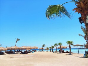 A beach with thatched umbrellas, palm trees, and sun loungers. - Cozy Studio with FREE Private Beach Access in Tiba Golden Resort (Hurghada)