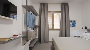 Et soveværelse med seng, skrivebord med stol, garderobeskab, et vindue med gardiner og et maleri på væggen.
