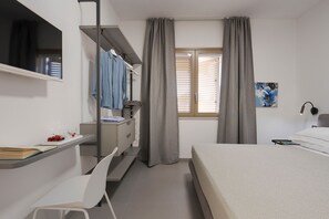 Ein Schlafzimmer mit Bett, Schreibtisch und Stuhl, Kleiderschrank, einem Fenster mit Vorhängen und einem Bild an der Wand.