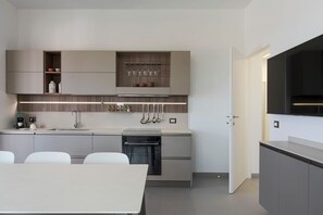Une cuisine moderne dotée d’appareils électroménagers intégrés, un coin repas avec une table et des chaises, et un téléviseur aux couleurs sombres fixé au mur.