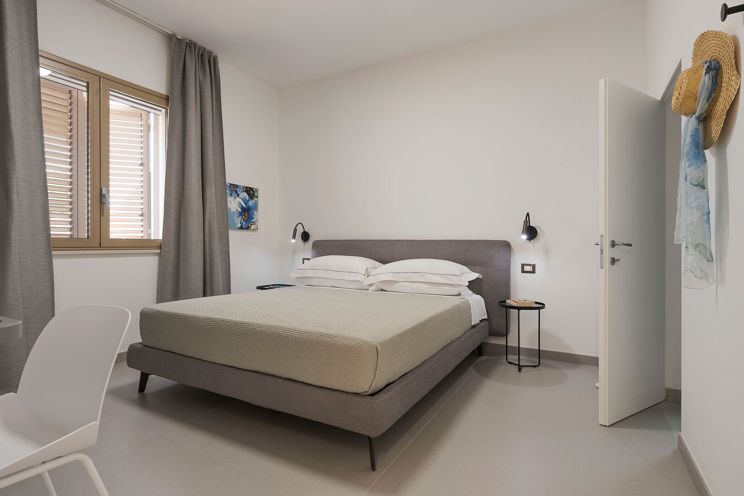 A bedroom with a bed, a chair, a bedside table, a door, and a window with curtains.