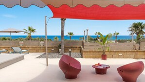 En terrasse ved stranden med moderne møbler, et bord med magasiner og havudsigt.