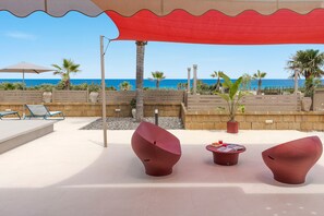 Eine Terrasse direkt am Strand mit moderner Sitzgelegenheit, einem Tisch mit Zeitschriften und Blick auf das Meer.
