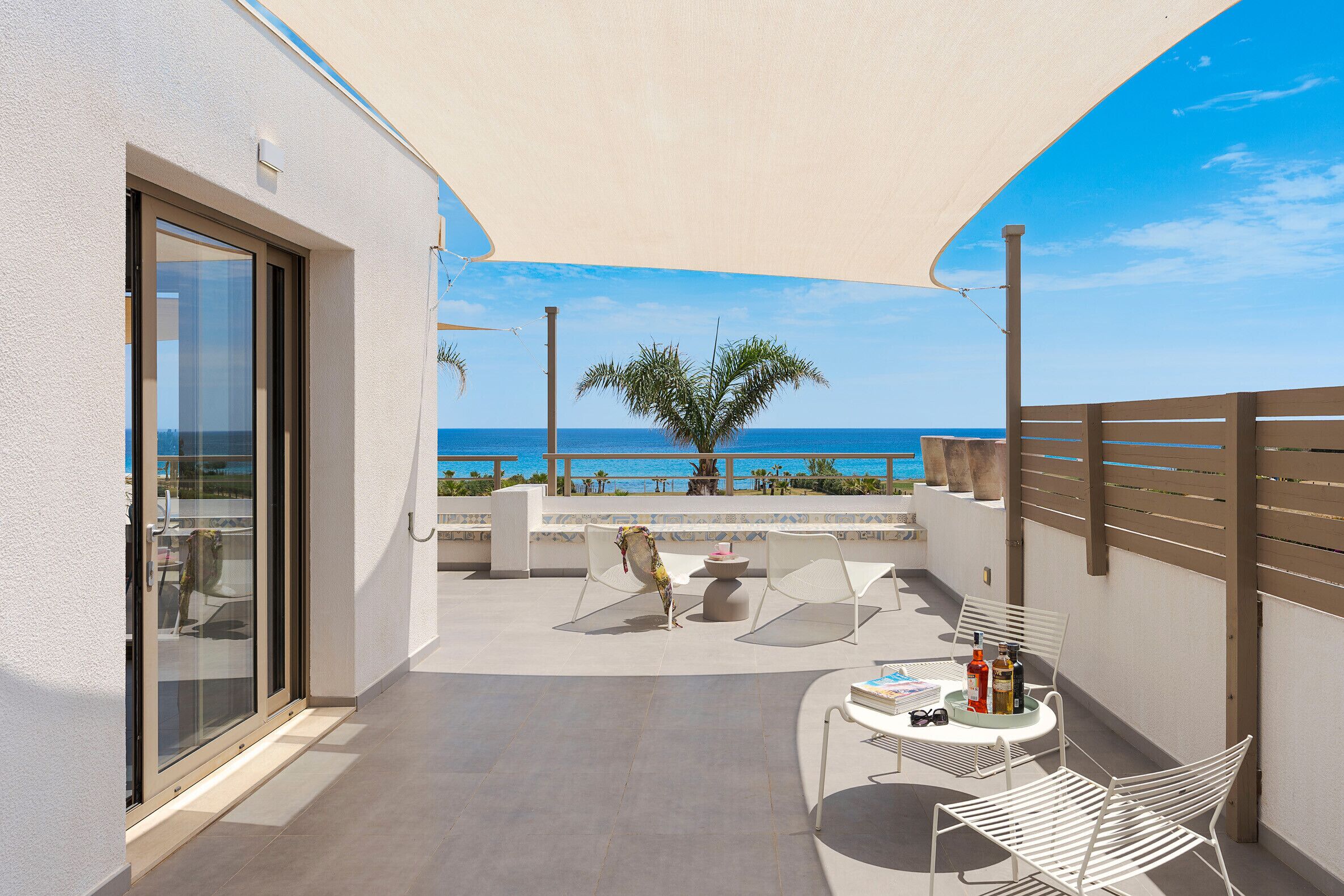 Een balkon met een tafel, stoelen en uitzicht op zee.