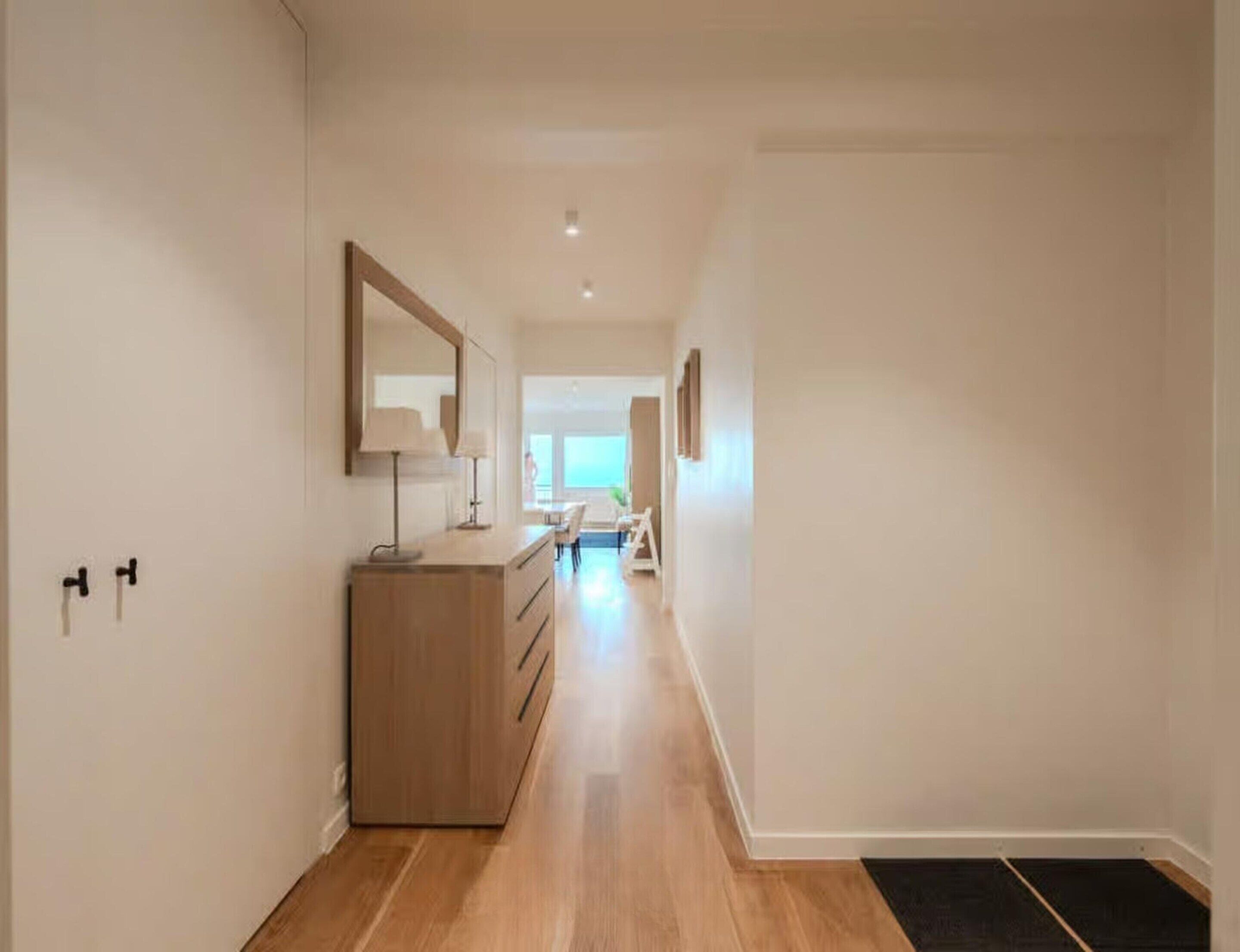 Un couloir avec une commode en bois, un miroir et un banc au fond.