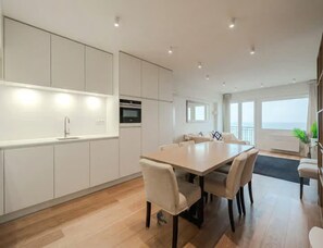 Eine moderne Küche mit integrierten Geräten, eine Essecke mit großem Tisch und Stühlen sowie Meerblick durch große Fenster.