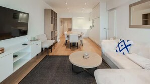 Una sala de estar moderna con un televisor de pantalla plana, un sofá, una mesa de centro y un comedor al fondo.