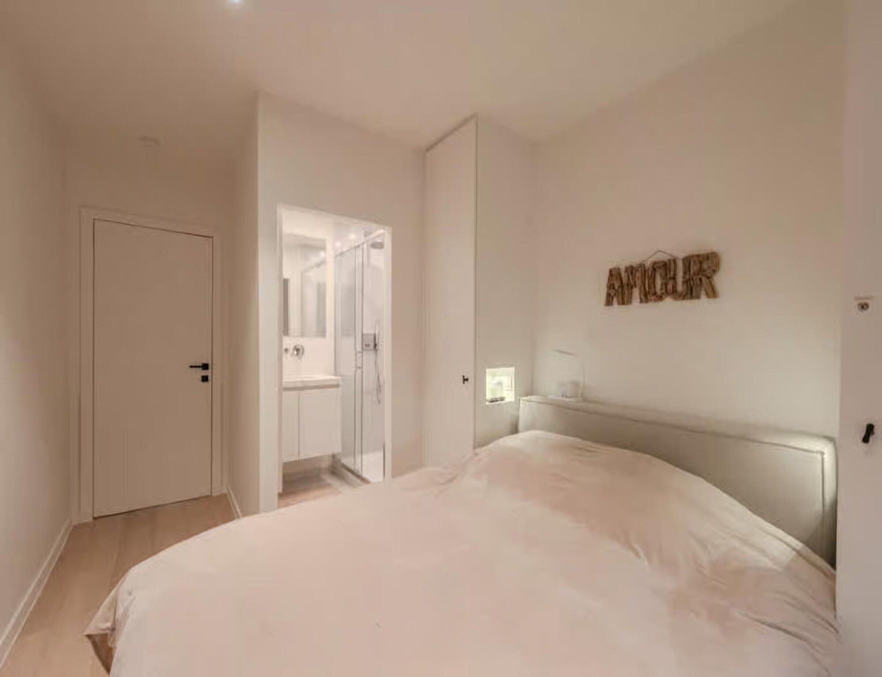 A bedroom with a bed, a door, a shower, and a wall-mounted light fixture.
