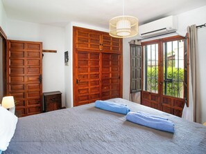 A bedroom with a large bed, wooden wardrobe, and a window with a view of greenery. - Vacation home Carmen by Interhome (Nerja)