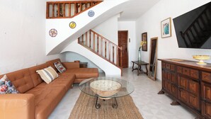 A living room with a brown leather sofa, a glass coffee table, a woven rug, a wooden staircase, and a wooden cabinet with a TV. - Vacation home Carmen by Interhome (Nerja)