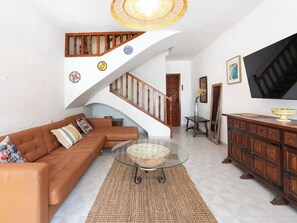 A living room with a brown leather sofa, a glass coffee table, a woven rug, a wooden staircase, and a wooden cabinet with a TV. - Vacation home Carmen by Interhome (Nerja)
