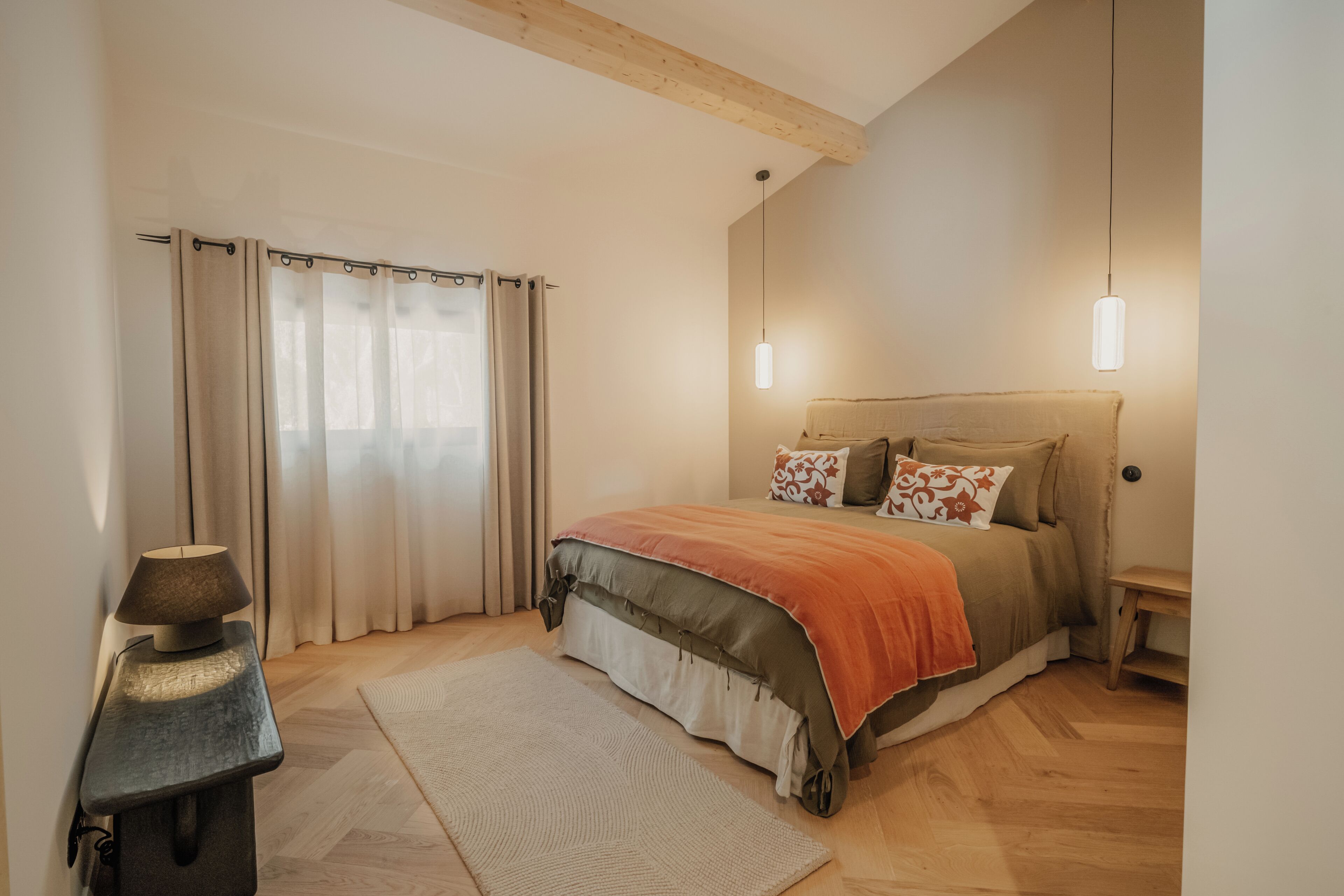 Een slaapkamer met een bed, gordijnen, een lamp, een vloerkleed en een nachtkastje.