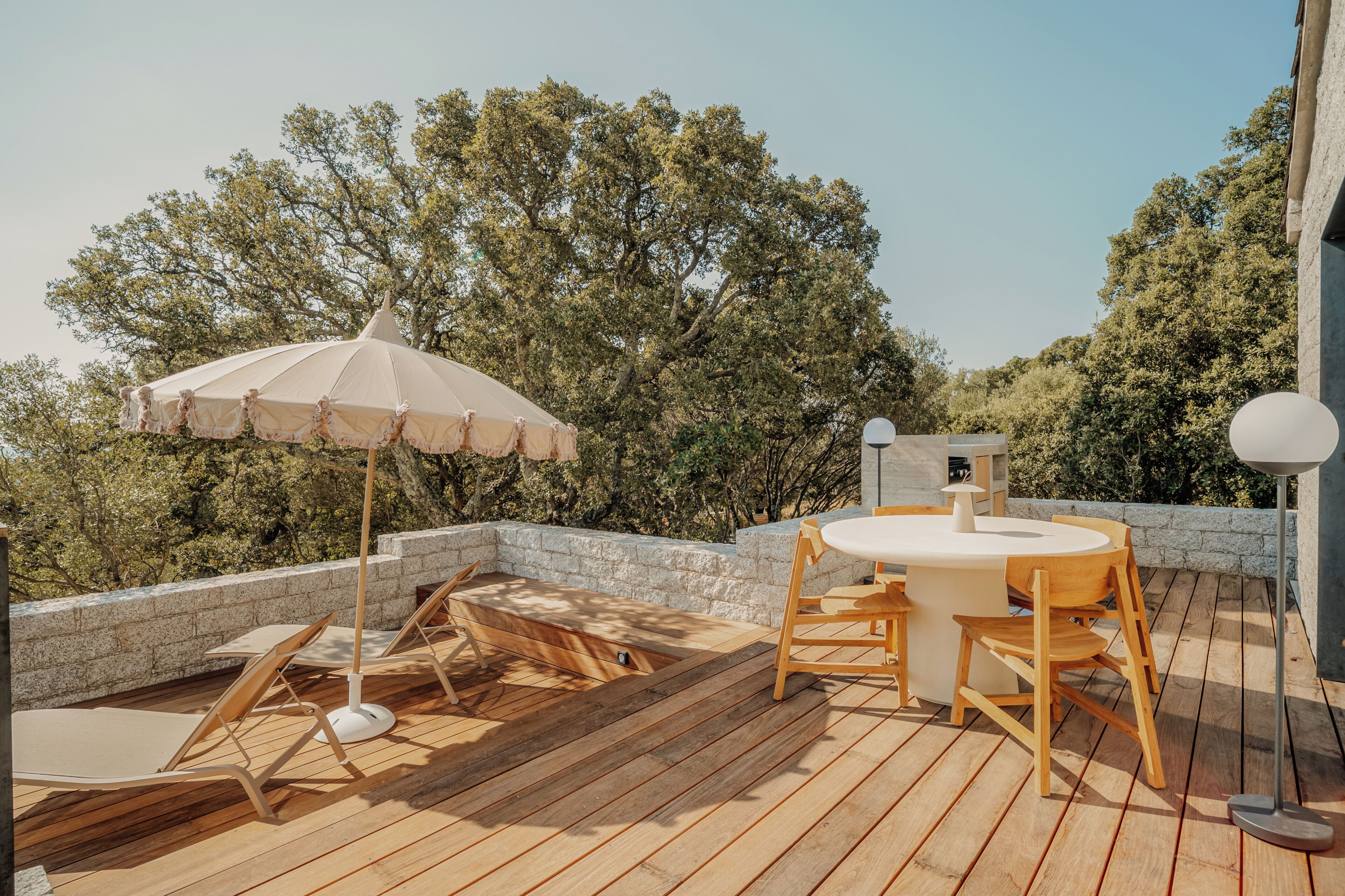 A wooden deck with a round table and chairs, an umbrella, and a stone wall.