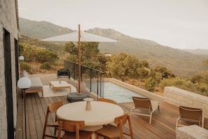 Eine Holzterrasse mit Gartenmöbeln, einem Pool und Blick auf Berge.