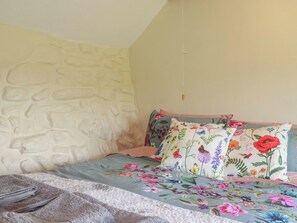 A bedroom with a stone wall, floral bedding, and a hanging light fixture. - Moorland Retreat (Bodmin)