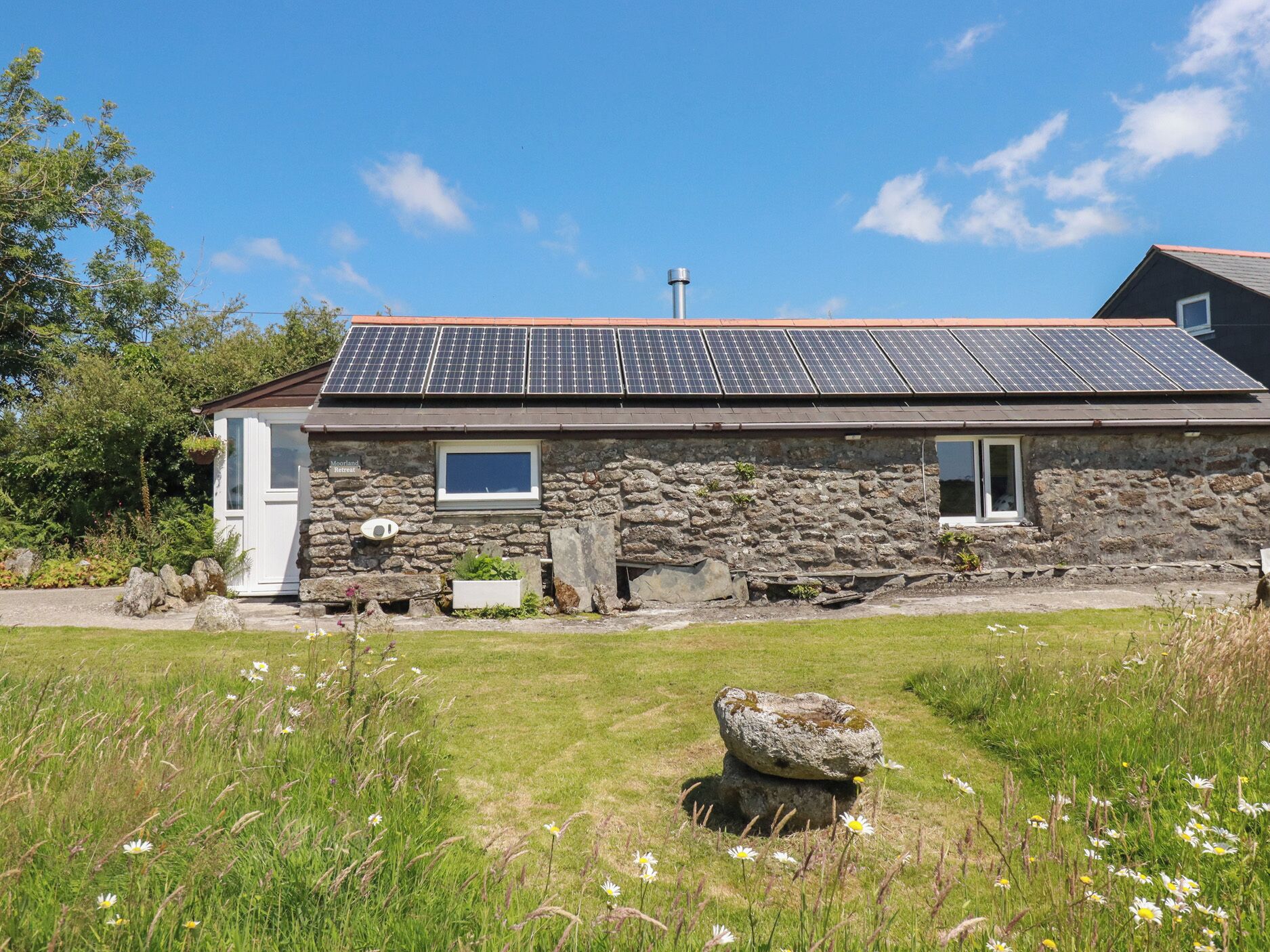 Edificio de piedra con techo solar, una ventana pequeña y un letrero que dice 'Moorland Retreat'.