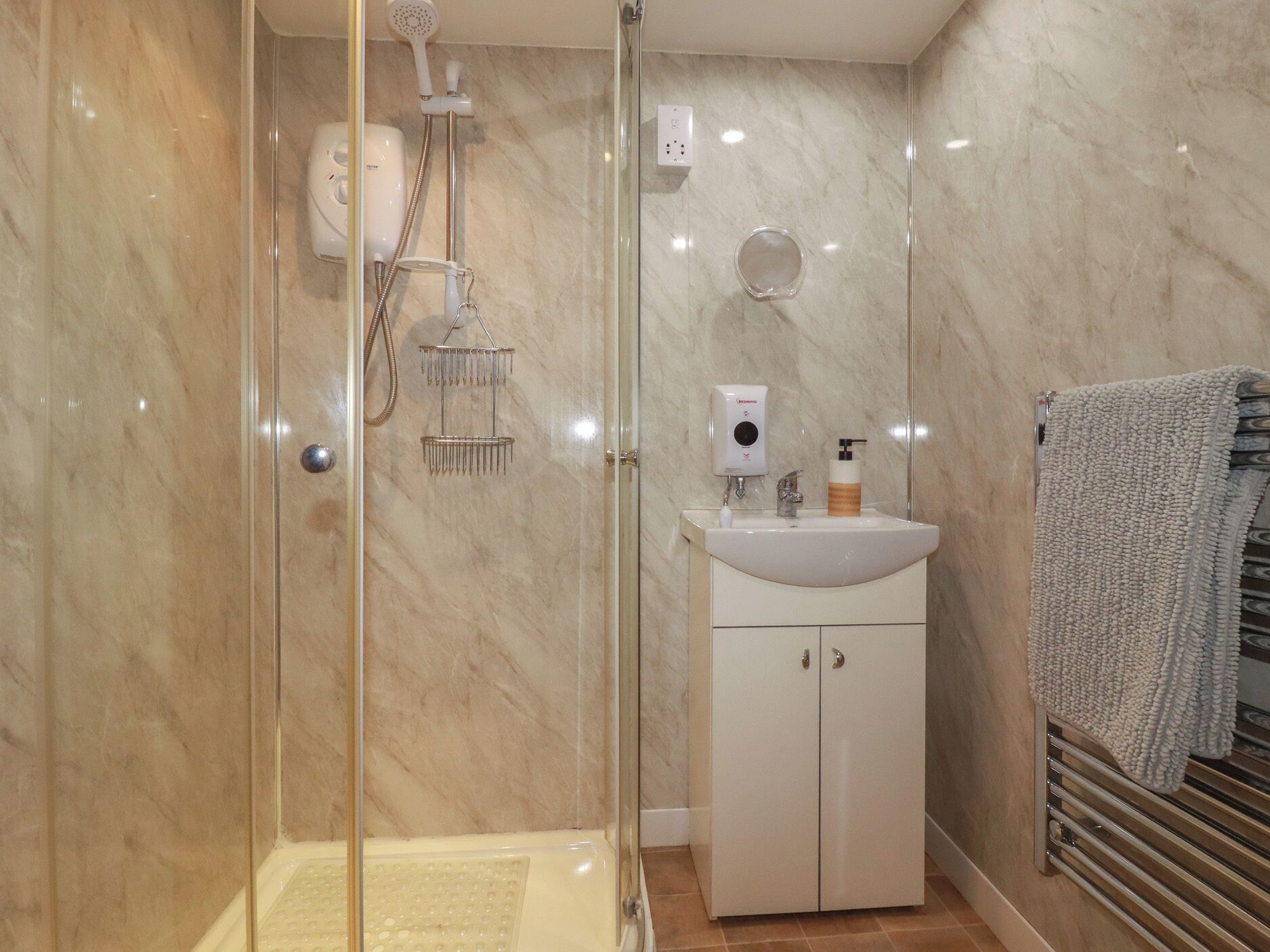 A modern bathroom with a glass-enclosed shower, a white sink with a soap dispenser, and a towel rack.