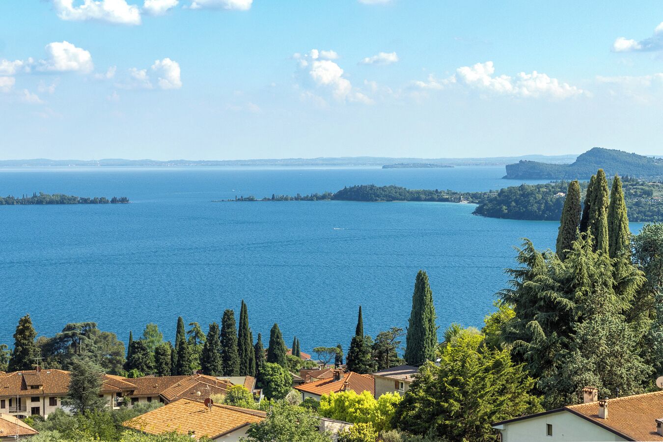 A coastal view with a clear sky, a large body of water, and a cluster of buildings with red-tiled roofs.