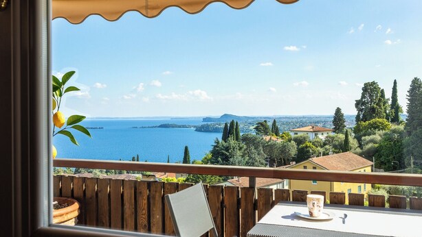 Varanda com vista para a água, cerca de madeira e uma mesa com uma xícara.