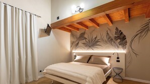 Quarto com cama, TV fixada na parede, luminária no teto e um mural decorativo.
