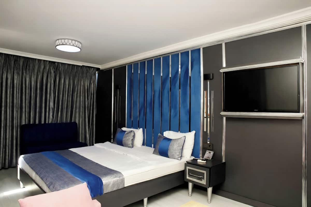 Quarto de hotel moderno com uma cama grande, televisão de tela plana, mesa de cabeceira e um divisor de ambiente em cortina.