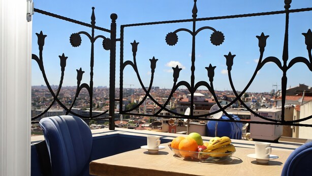 Un balcon avec une balustrade en métal, une table sur laquelle se trouve un saladier rempli de fruits et une chaise.