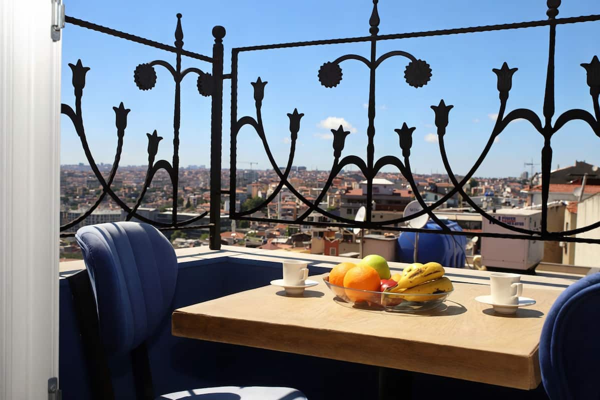 Uma varanda com grades de metal, uma mesa com uma tigela de frutas e uma cadeira.