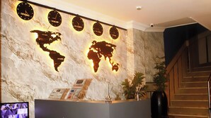 Un comptoir d’accueil avec une carte du monde et des horloges, un escalier et un écran de télévision.