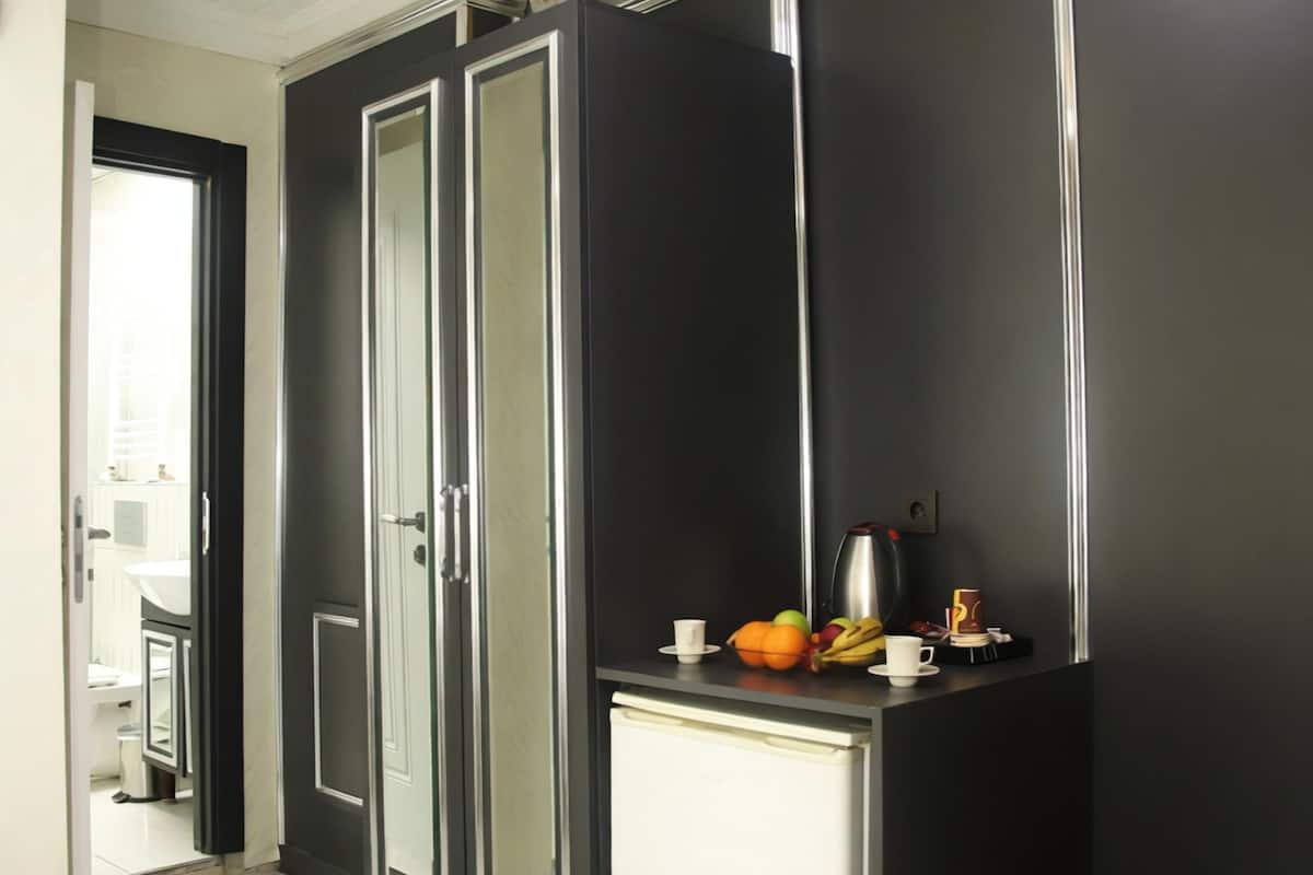 Quarto com guarda-roupa, uma mesinha com frutas e uma cafeteira, e um cesto de lixo.