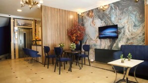 Un hall d’hôtel moderne avec un mur en marbre, un téléviseur à écran plat, un canapé bleu et un coin repas avec des chaises et une table.