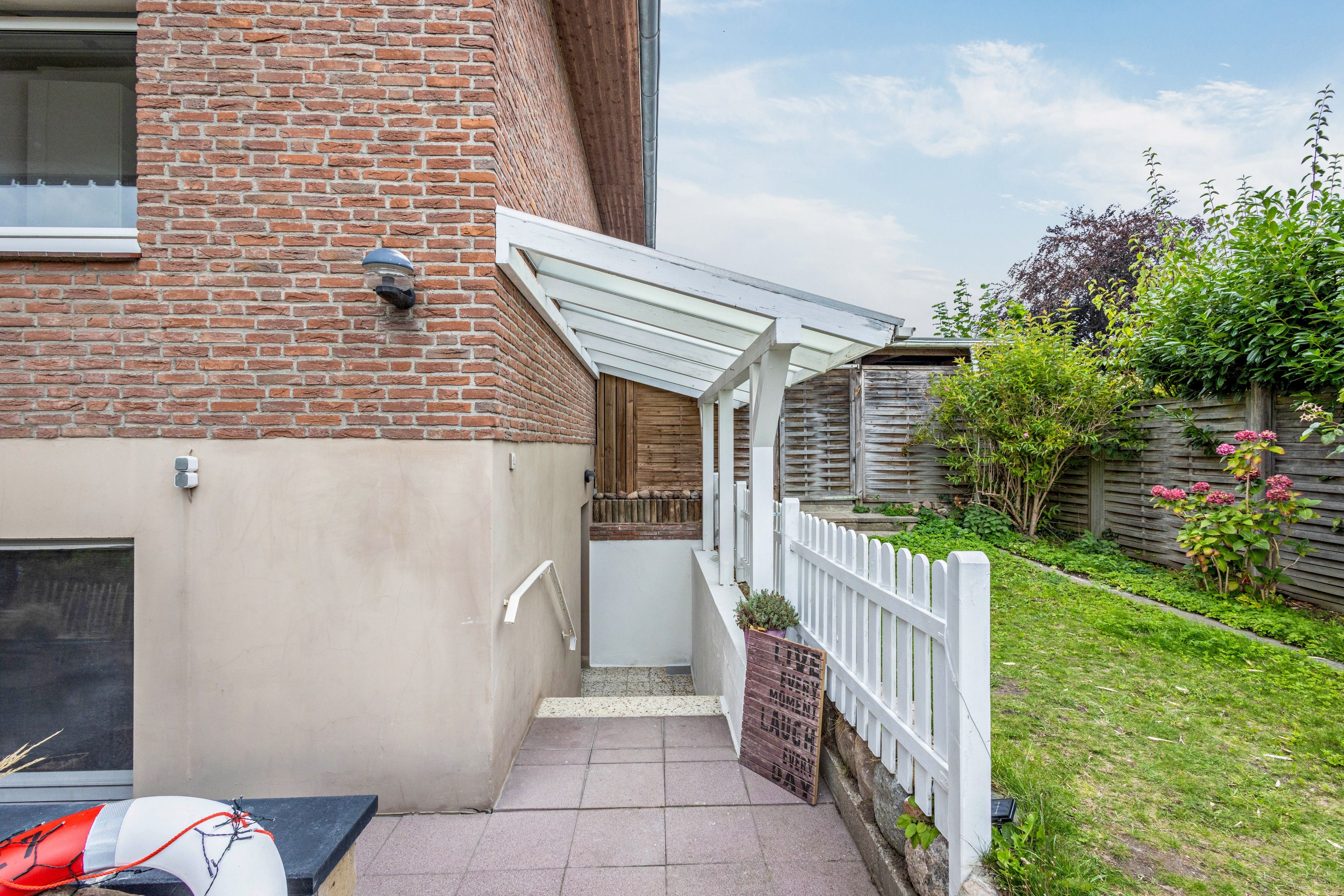 Ein Ziegelhaus mit weißem Veranda und Holzzaun.