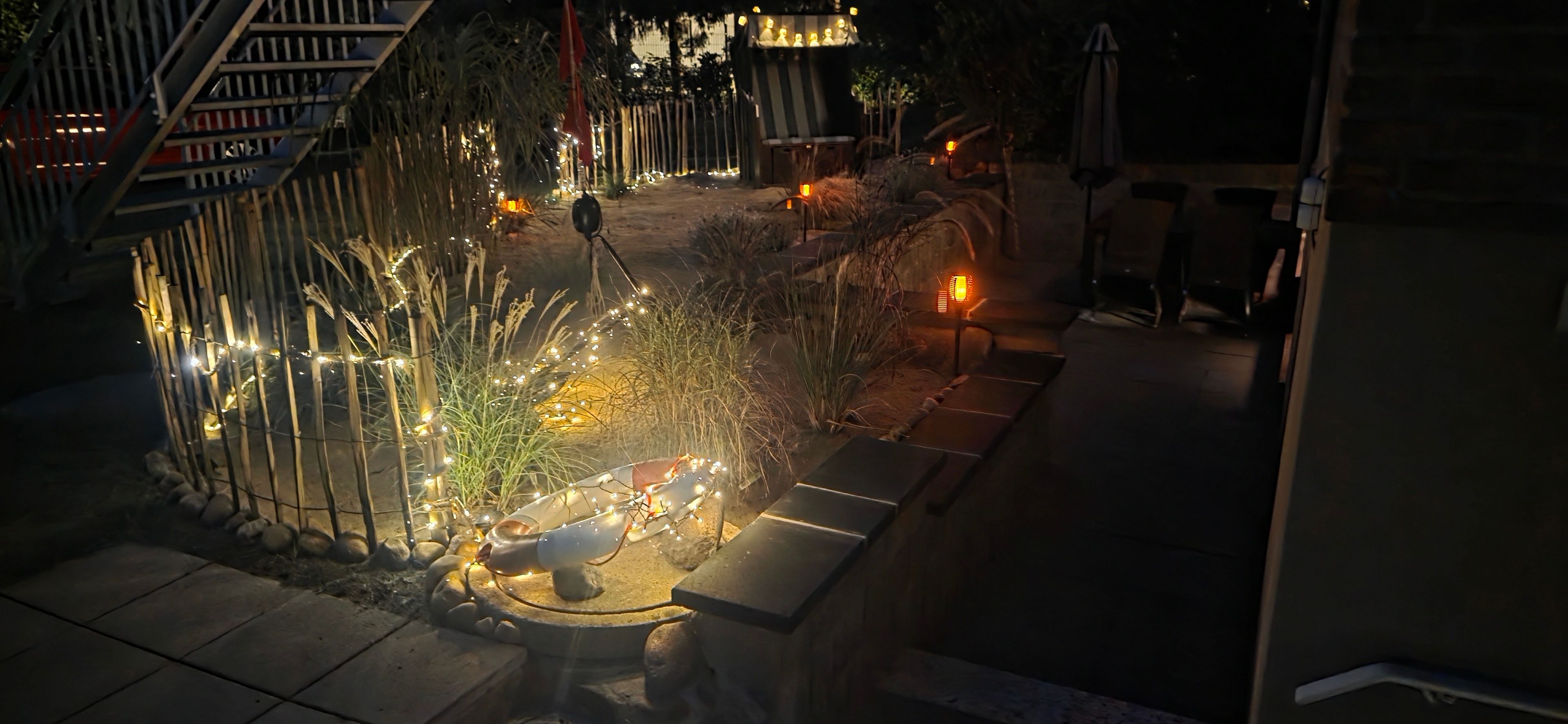 A nighttime outdoor area with a pathway, decorative lights, and a small seating area.