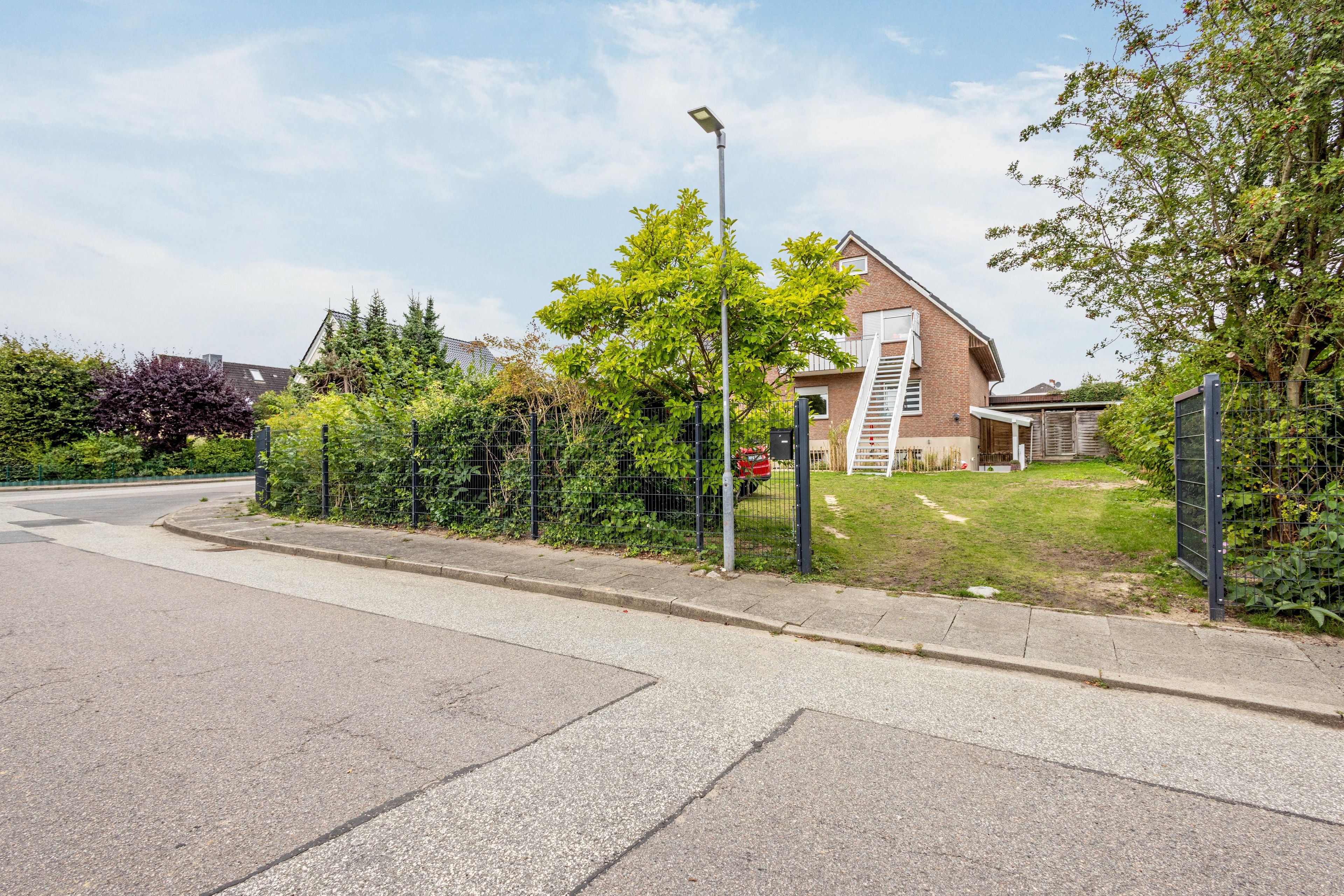 A residential street with a house, a fenced garden, and a street lamp.