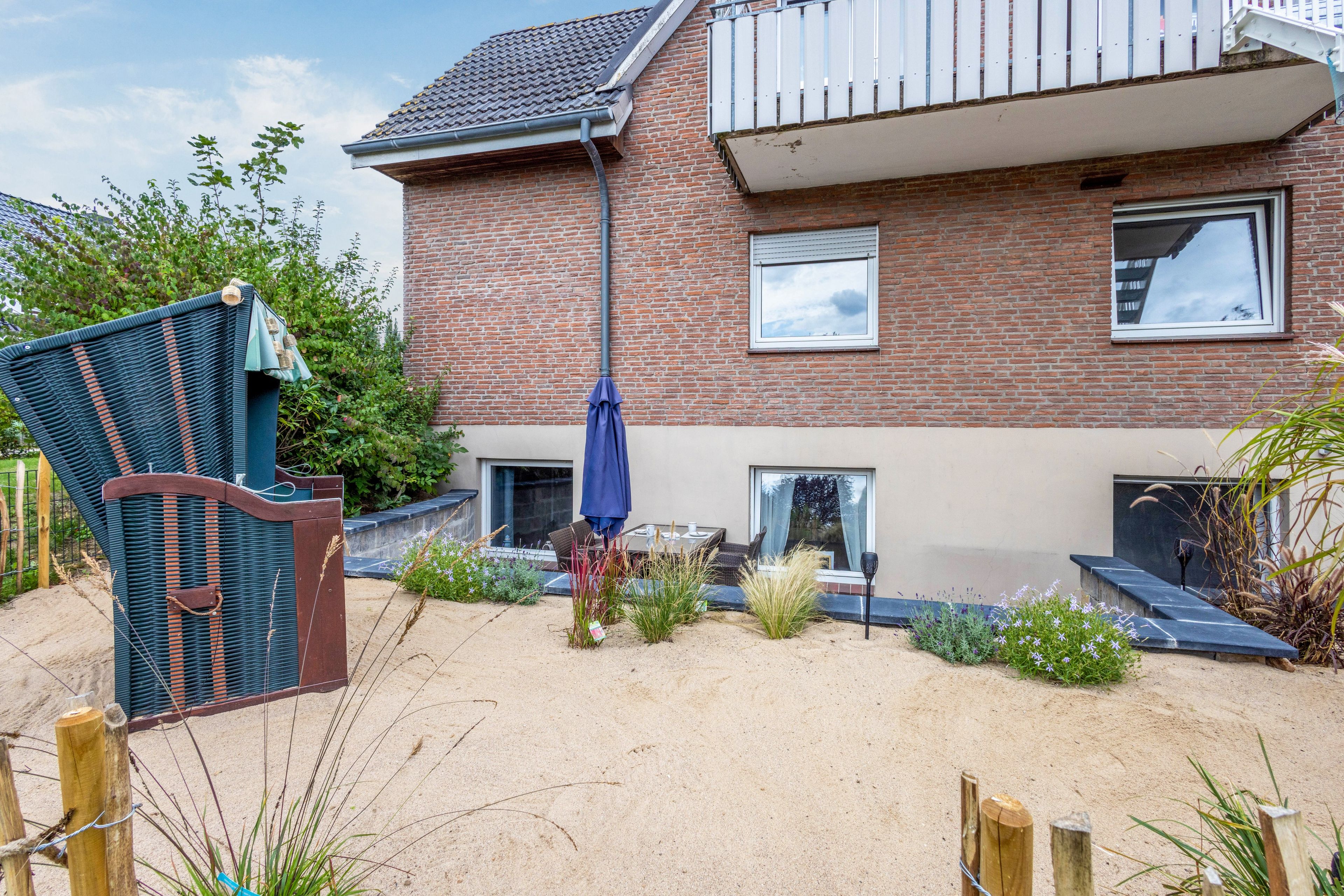 A brick house with a garden, a blue umbrella, and a wicker chair.