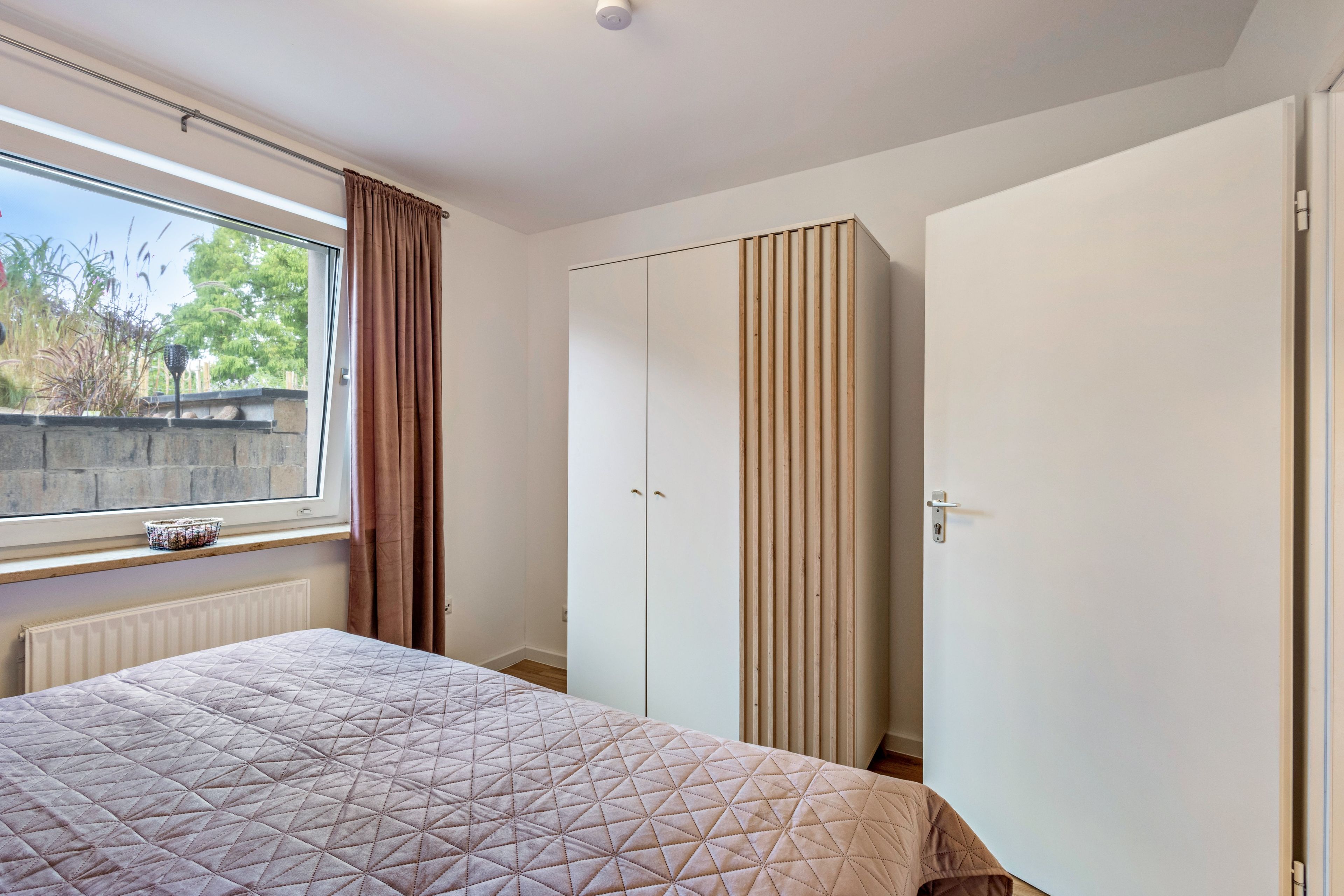 Un dormitorio con cama, ventana con cortinas, radiador y armario.