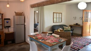 A kitchen with a refrigerator, a dining table with chairs, a wicker chair, a sofa, and a patterned rug. - Konka Guest Farm (Carnarvon town)