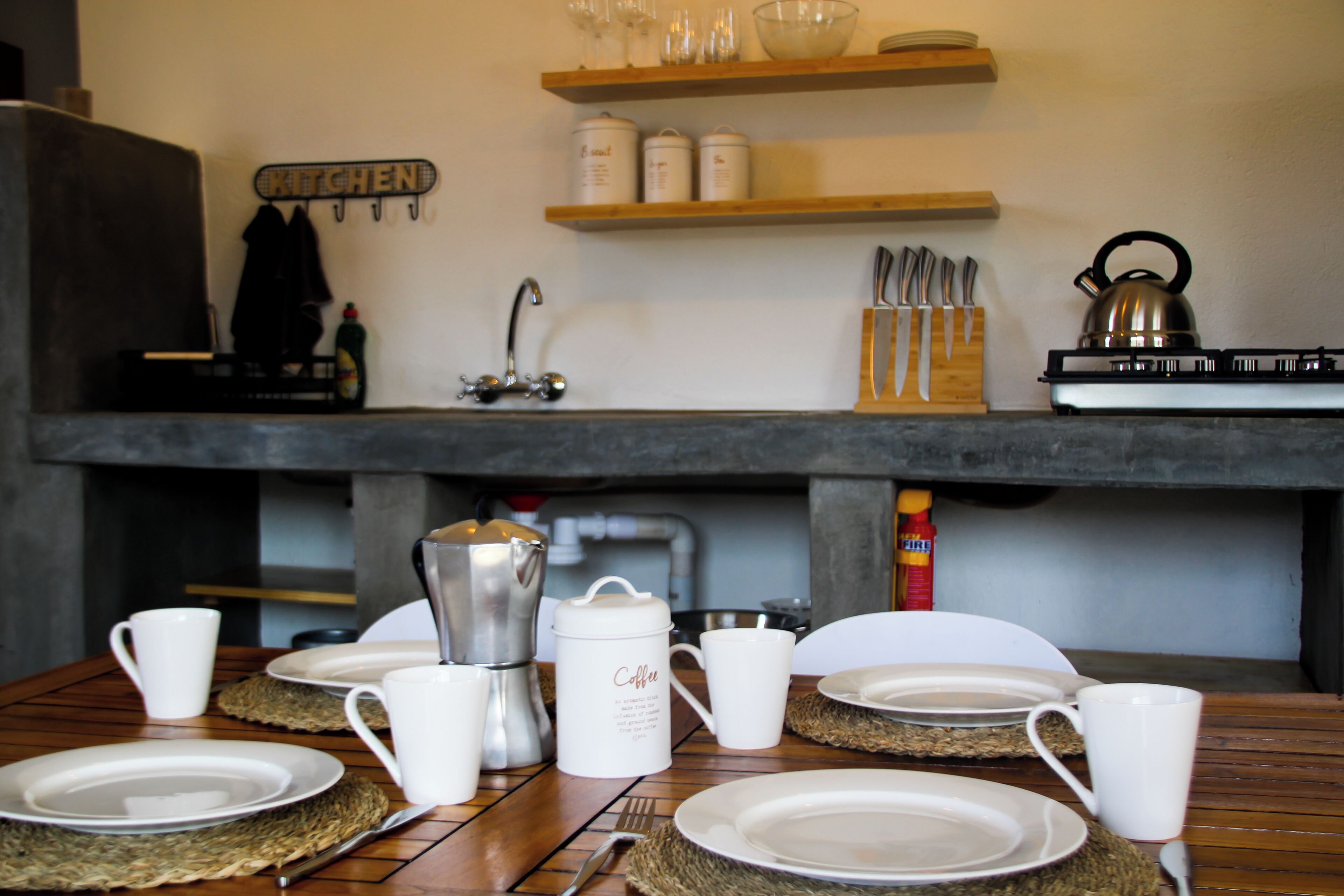 A kitchen area with a coffee maker, utensils, and a kettle on the counter.