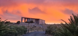 A building with a sloped roof and multiple windows, surrounded by dry vegetation and a dirt path. - Konka Guest Farm (Carnarvon town)