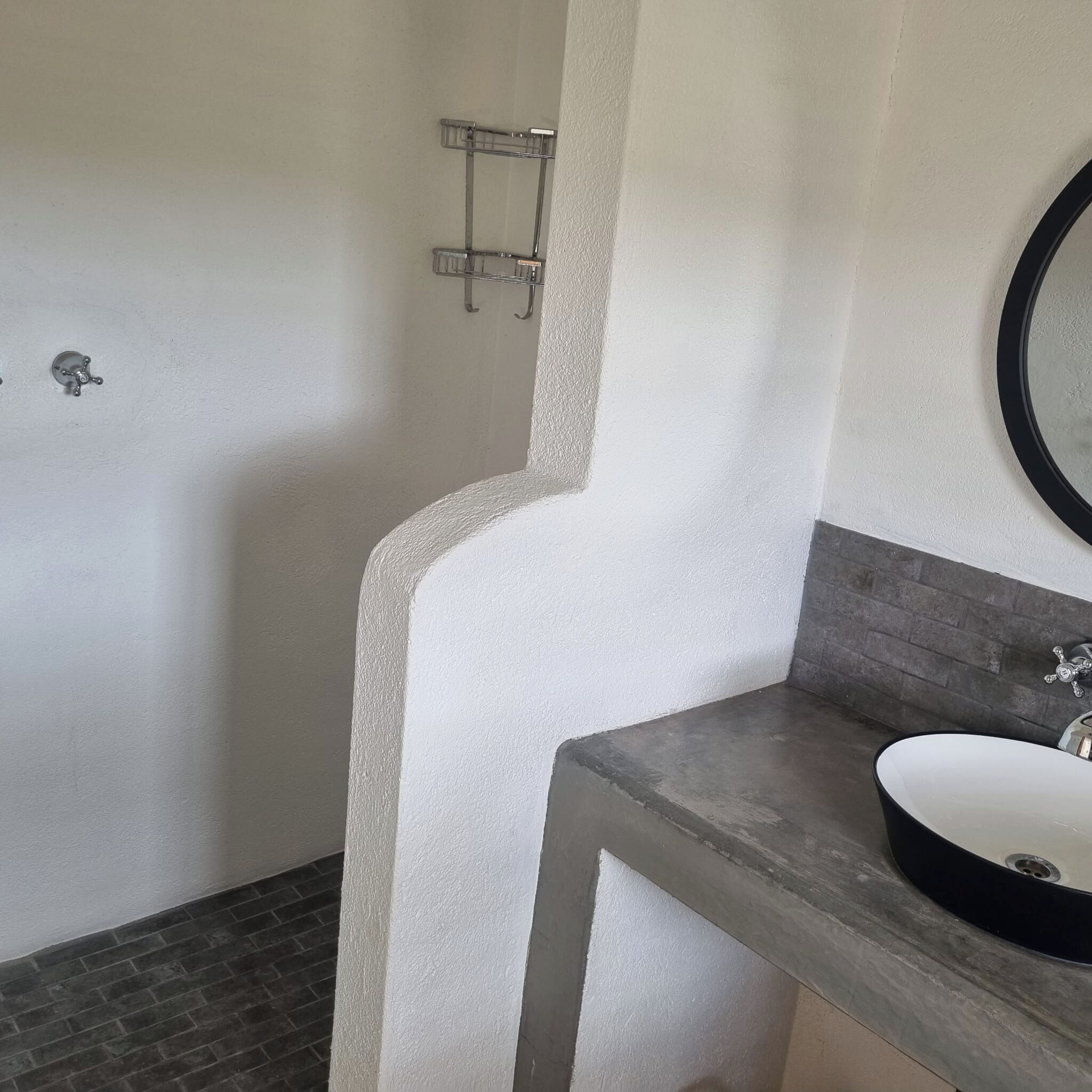 Ein Badezimmer mit weißer Wand, grauem Boden, einem runden Spiegel und einem Waschbecken.