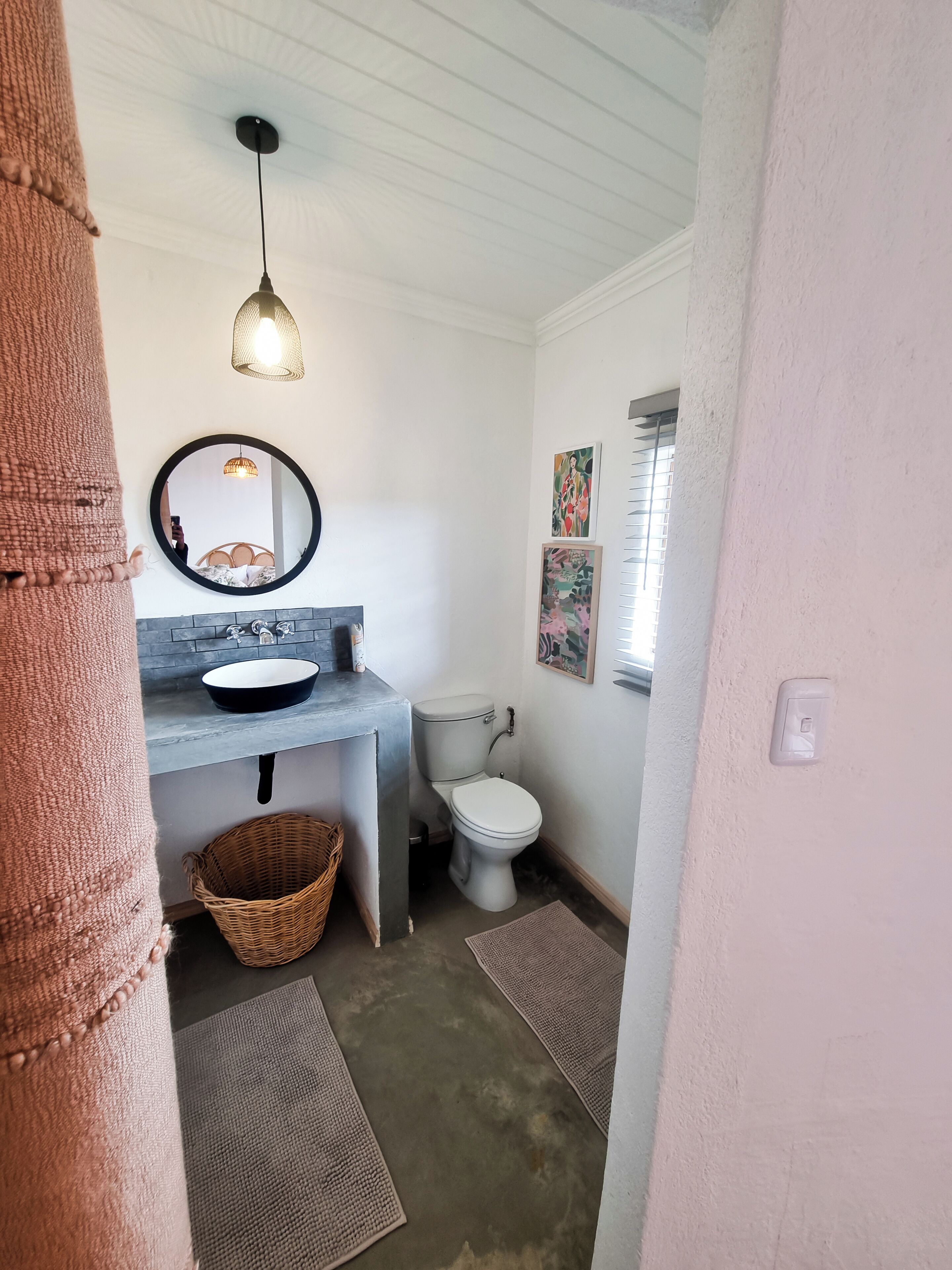 Un baño con espejo redondo, lavamanos, inodoro e iluminación colgante.