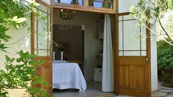 Uma porta de madeira dá acesso a um quarto com uma cama, um candelabro e uma janela.