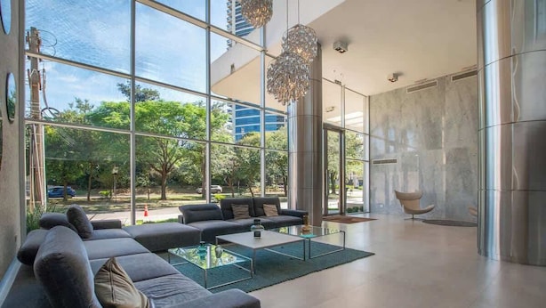 A modern interior with large windows, a sectional sofa, a coffee table, and a hanging light fixture. - Corporate Stays Sky Tower - 807  (Asunción)