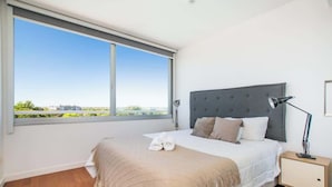 A bedroom with a large window, a bed with a grey headboard, a bedside lamp, and a view of the city. - Corporate Stays Sky Tower - 807  (Asunción)