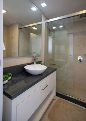 Un baño moderno con un lavabo blanco, un espejo grande y una cabina de ducha de vidrio.