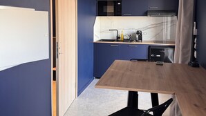 Pieni, käytännöllinen keittiö, jonka seinät ovat tummansiniset, ja jossa on puinen ruokapöytä sekä musta tuoli.