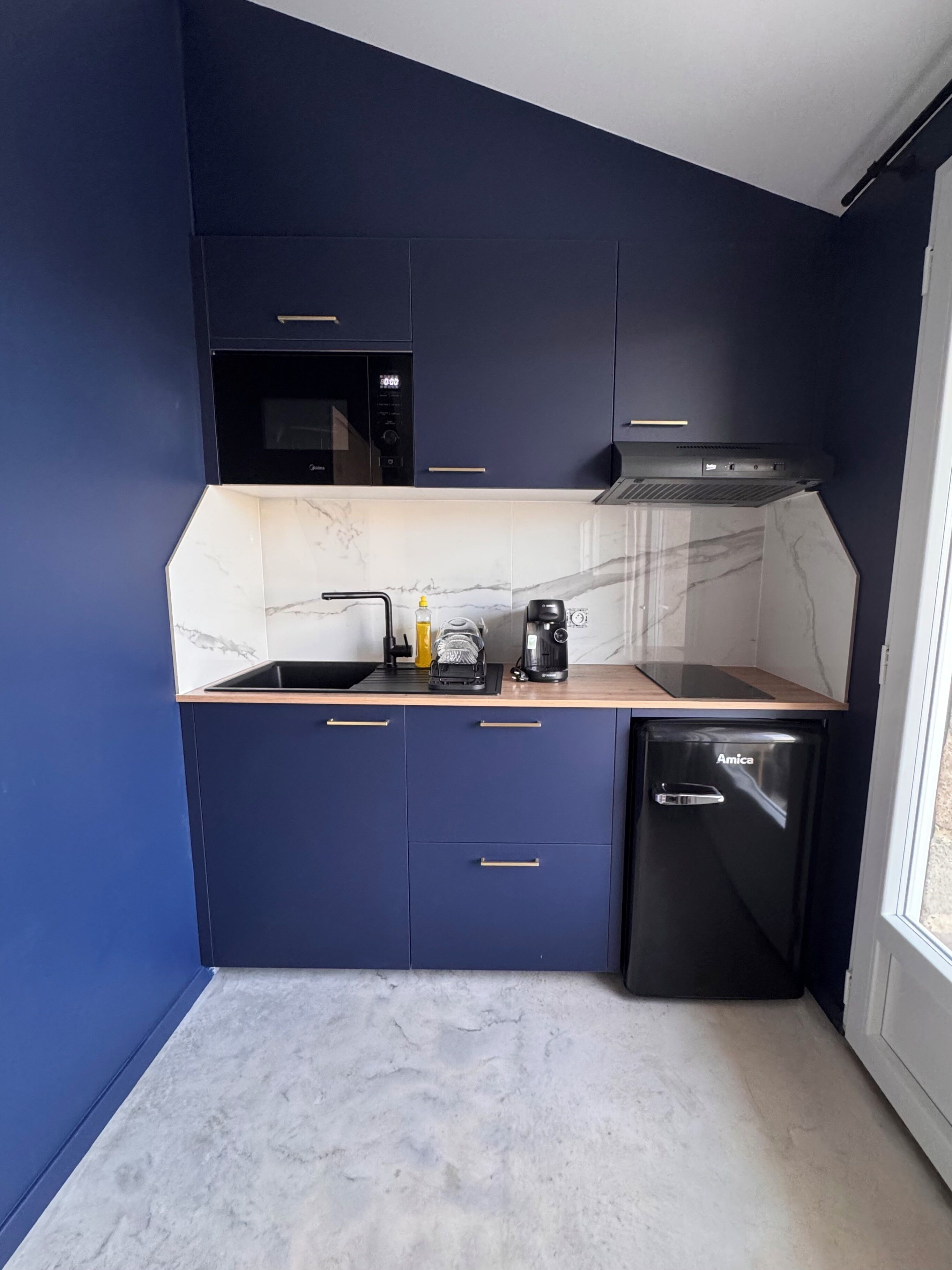A compact kitchen with dark blue cabinets, a microwave, a coffee maker, and a dishwasher.