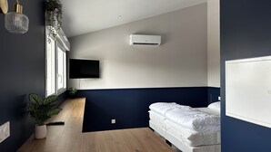 Moderni hotellihuone, jossa on sänky, taulutelevisio, ilmastointilaite ja ruukkukasvi.