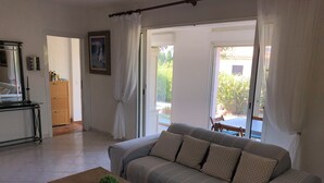 Een woonkamer met een bank, een houten salontafel met een plant, een eettafel en een keukenhoek.